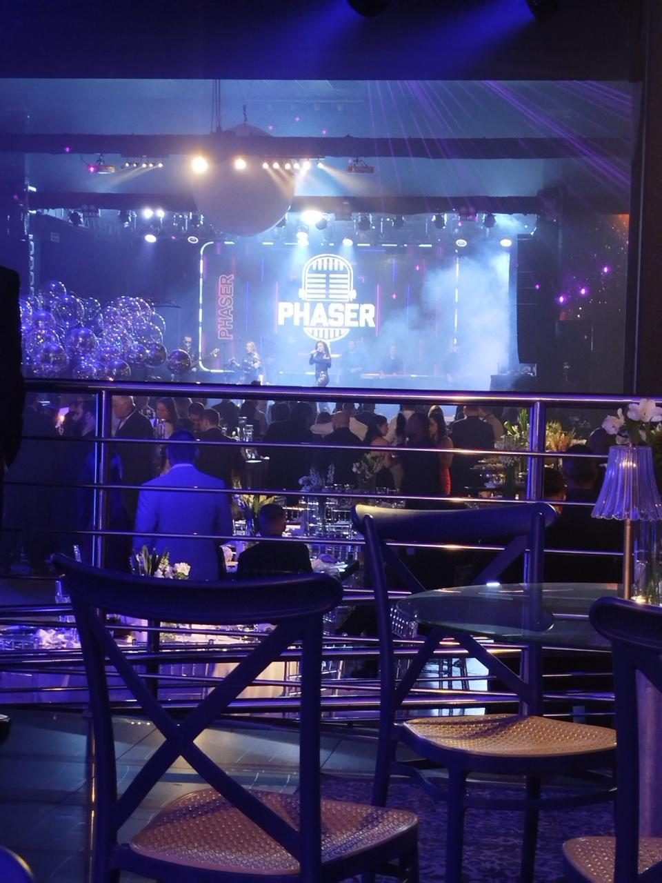 Evento corporativo de gala com painel de LED, iluminação cênica azul e convidados em mesas decoradas
